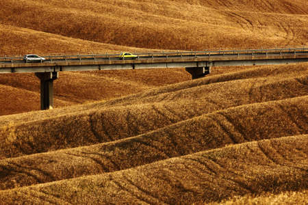 Wavy breown hillocks, sow field, agriculture landscape, bridge with two cars, nature carpet, Tuscany, Italyの写真素材