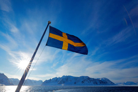 Sweden flag with blue sky. Rocky island with snow. White snowy mountain, blue glacier Iceberg twilight, ocean. Pink clouds with ice floe. Beautiful landscape. Land of ice. Cold blue water nature.の写真素材