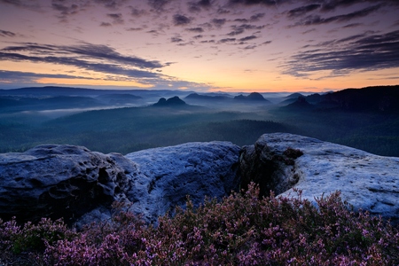 Kleiner Winterberg, beautiful morning view over sandstone cliff into deep misty valley in Saxony Switzerland. Sandstone peaks increased from foggy background, fog is orange due to sunrise, Germany.の写真素材