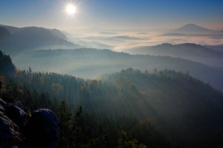 Forest with sun rays. Morning with sun. Cold misty foggy morning in a fall valley of Bohemian Switzerland park. Hills with fog, landscape of Czech Republic, sun beam in the landscape Ceske Svycarsko. の写真素材