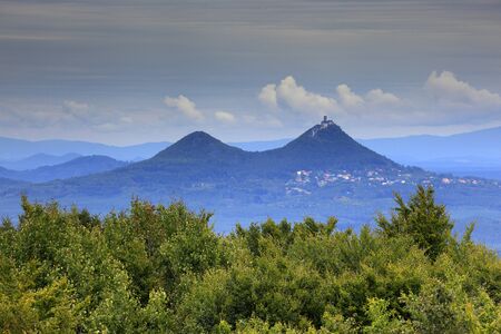Bezdez Hill, in Kokorinsko mountain, Czech Republic. Hill with clouds. Beautiful morning landscape. Village below the hill. Landscape with fields and meadow around  mound. Sky before storm.の写真素材