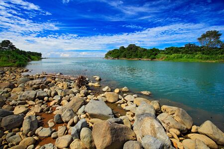 Beautiful river landscape from Costa Rica. River Rio Baru in the tropic forest. Stones in the river. Trees above the river. Summer river with blue sky. Typical landscape in the tropic green forest. の写真素材