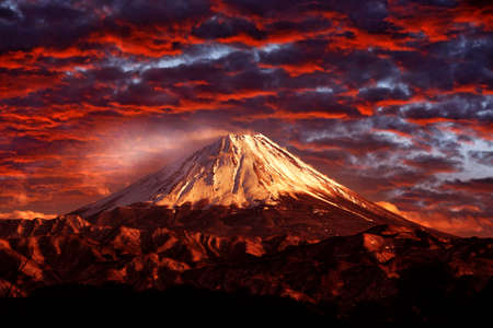 Volcano Fuji during beautiful sunset, red clouds on the sky. Active hill with eruption, twilight in Japan. Mount Fuji, San, orange evening in Asia landscape. Volcan traveling in Japan.の写真素材