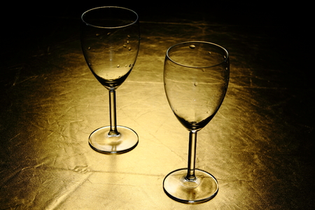 Two wet wine glasses on the table with golden surface and spotlightの写真素材