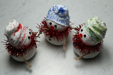 Three textile snowmen with colorful caps on the gray-white floorの写真素材