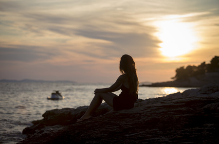 pretty girl sitting on seashore at sunsetの写真素材