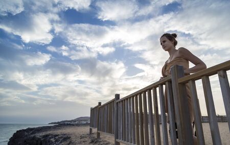 A woman looks off into the distance on ocean and leaning on the railing, beautiful skyの写真素材