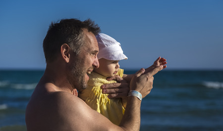 father with little daughter on the hands by the sea looking into the distanceの写真素材
