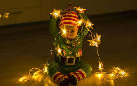 Santa helper baby on the floor decomposes Christmas lights that are shaped like starsの写真素材