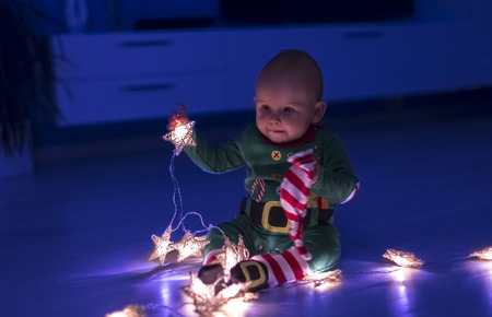 Santa helper baby on the floor decomposes Christmas lights that are shaped like starsの写真素材