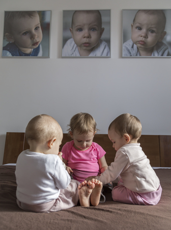 Three little sisters play on the bed and their portraits hang on the wallの写真素材