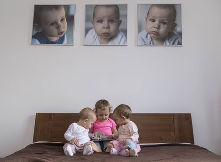 Three little sisters play on the bed and their portraits hang on the wallの写真素材
