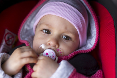 Beautiful 1 year old baby in a stroller attached in a car seat. Outdoors in cold weatherの写真素材