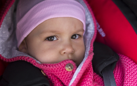 Beautiful 1 year old baby in a stroller attached in a car seat. Outdoors in cold weather