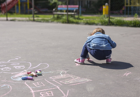 Little beautiful girl in a jeans jacket draws with colored chalks on the playgroundの写真素材