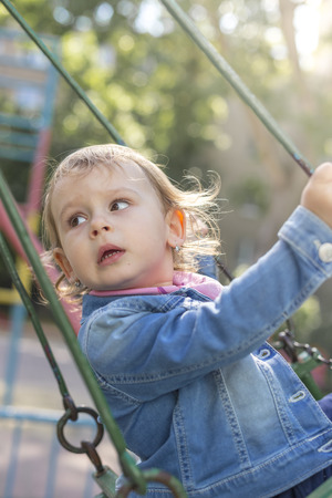 A two-year-old girl moves on a swing in the park while looking dangerously behind her backの写真素材