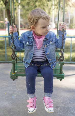 Beautiful little girl sitting securely chained on a swingの写真素材
