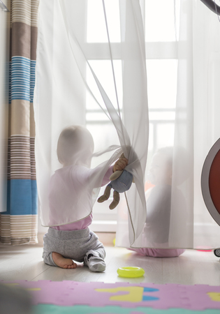 twins play with a curtain at home on the floor, in front of the balcony windowの写真素材