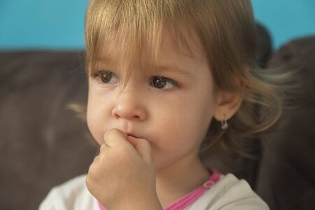 a beautiful little girl looks sad with her fingers in her mouthの写真素材