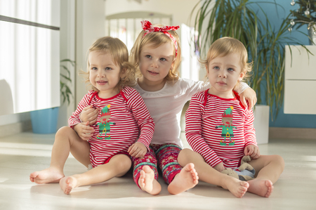 twins and older sister sitting at home on a bright floor in Christmas Santa's helper attireの写真素材