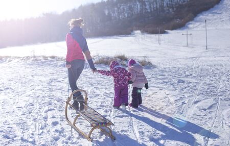 In the winter on a sunny day, the mother with two children walks up the hill and pulls behind the sledgeの写真素材