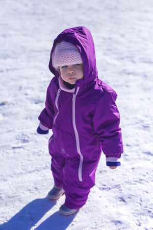 Adorable girl with blue eyes in a  white snow warm suit playing in snow on a sunny winter day in a parkの写真素材