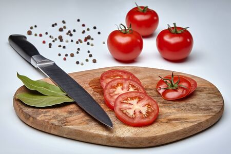 Slices of ripe tomatoes on a cutting board with a knife and three whole tomatoes nearbyの写真素材