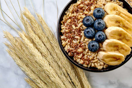 Whole oatmeal porridge with blueberry banana slices in a dark bowlの写真素材