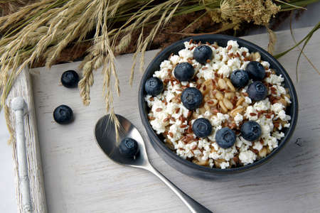 Whole grain oatmeal porridge with flax seeds and blueberries on a white vintage serving with a bouquet of dry herbsの写真素材