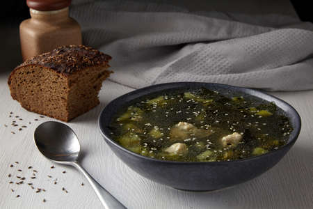 Rustic zucchini soup with meatballs with a piece of black bread with caraway seeds on a white table against the background of a gray towel kitchen. Village lunchの写真素材