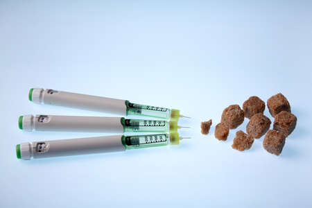 Insulin in syringe pens against brown sugar on a blue glowing table. Diabetes treatment concept