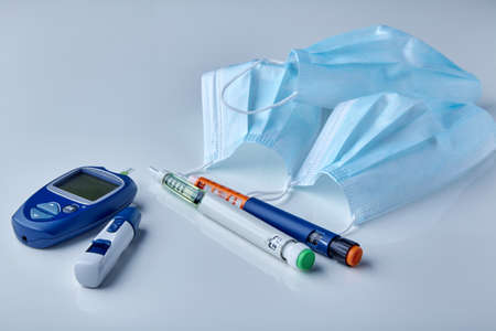 Insulin syringe pens, glucometer and medical masks on a white table. Risk of viral complications in...