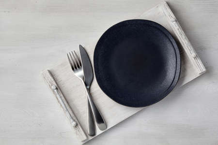 A dark ceramic plate and a tray of cutlery on a light wooden tableの写真素材