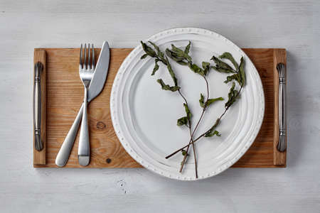 White ceramic plate and dry mint leaves and a tray with cutlery