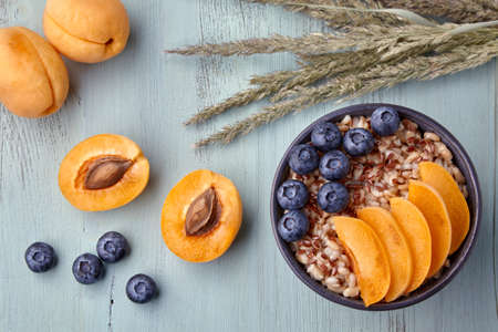 Whole grain oatmeal with apricot slices and blueberries on a wooden tableの写真素材