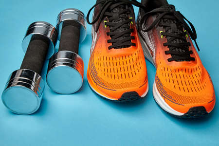 Orange sneakers and metal dumbbells on a blue backgroundの写真素材