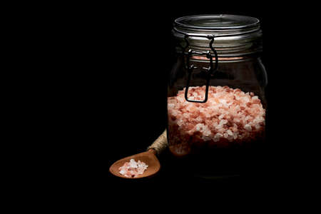 Pink himalayan salt on wooden spoon and glass jar photographed in dark key