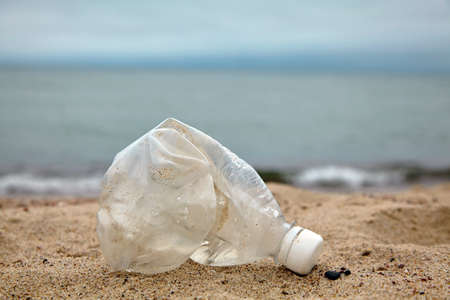 Crumpled plastic bottle on the sandy beach against the background of the sea Day Recycling