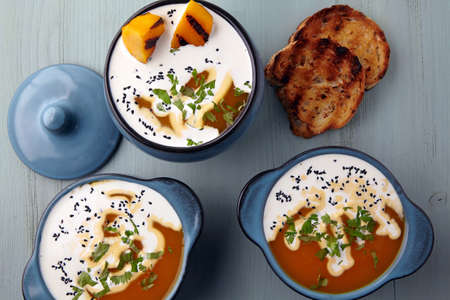 Pumpkin cream soup with cream, black cumin seeds, herbs and toasted bread on a light blue wooden...