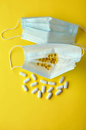 Medical masks and pills on a yellow background. Protection against viral infectionsの写真素材