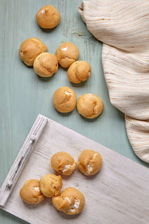 Appetizing profiteroles with whipped cream on a white wooden tray