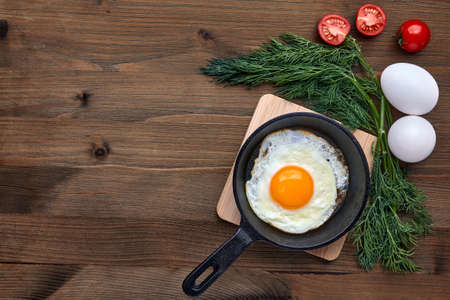Fried chicken egg in a small frying pan with a stand, a bunch of dill, tomatoes