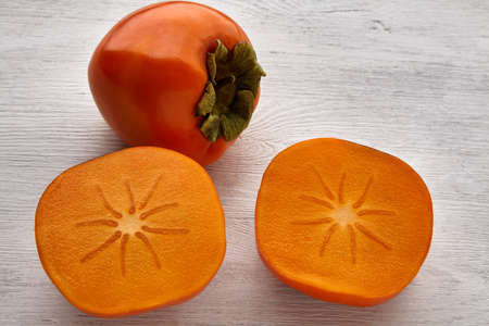 Ripe orange persimmon whole fruit and sliced sliced on a white wooden tableの写真素材