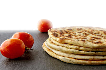 Flatbread with cheese and herbs on a dark stones plate with tomatoes