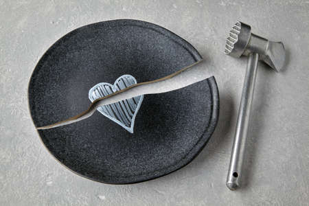 Broken ceramic plate with a painted heart and a kitchen hammer