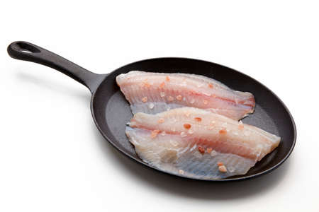 White fish fillet sprinkled with pink salt lies in a cast-iron frying panの写真素材