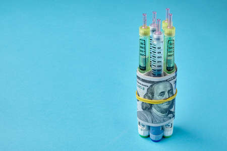 nsulin syringe pens wrapped in dollar bills on a blue backgroundの写真素材