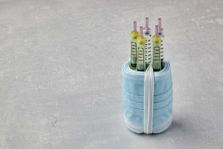 Insulin syringe pens wrapped in medical masks on a gray concrete background