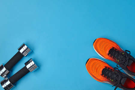 Orange sneakers and metal dumbbells on a blue background. Equipment and exercises for fitness....