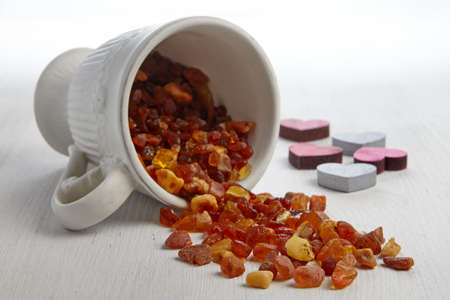 Raw amber in a white cup scattered on a wooden white table and wooden decorative heartsの写真素材
